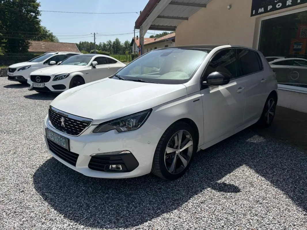 Peugeot 308 GT-Line blanche vue en 3/4 avant droit, avec jantes alliage et toit noir contrasté, stationnée sur gravier.