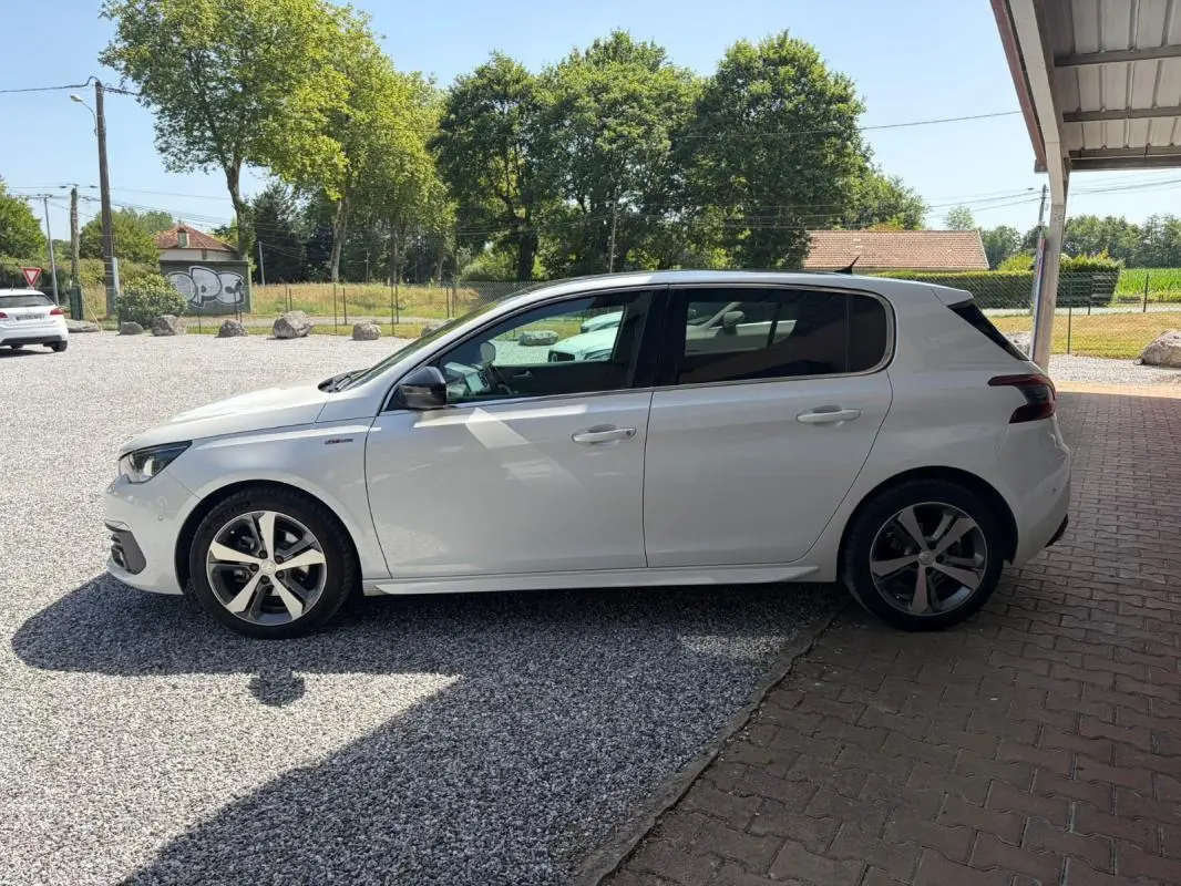 Peugeot 308 GT-Line blanc vue de profil côté gauche, avec jantes alliage et vitres teintées, stationnée à l'ombre.
