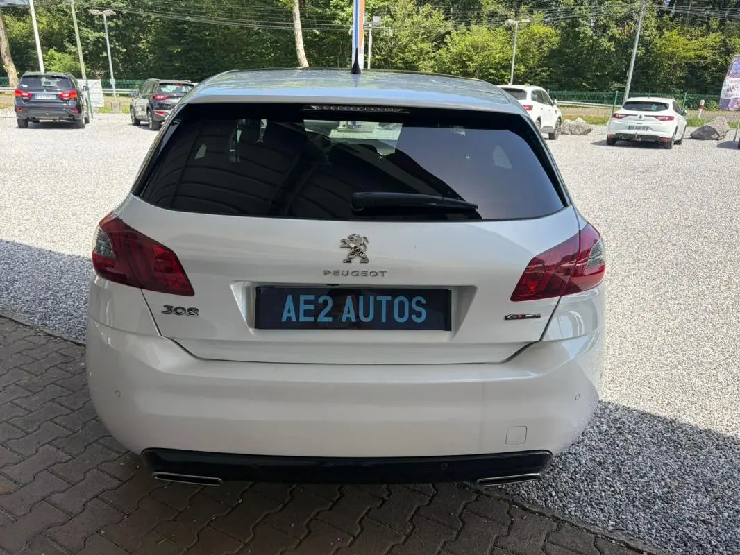 Vue arrière d'une Peugeot 308 GT-Line blanche de 2017, avec feux arrière rouges et double sortie d'échappement.
