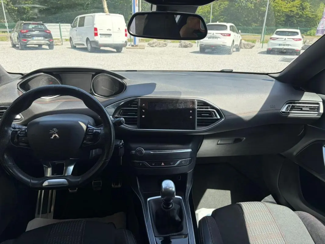 Vue intérieure avant du tableau de bord de la Peugeot 308 GT-Line blanche de 2017 avec volant compact et boîte manuelle.
