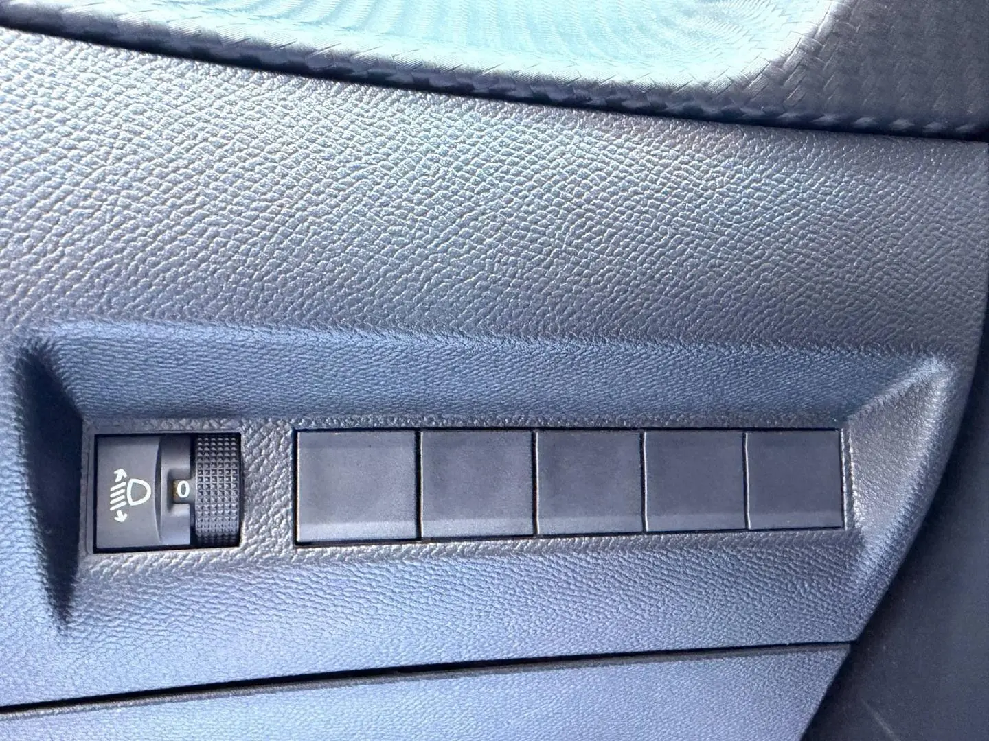 Gros plan sur le panneau de réglage des phares et boutons noirs sur la portière côté conducteur du Peugeot 208 gris Artense.