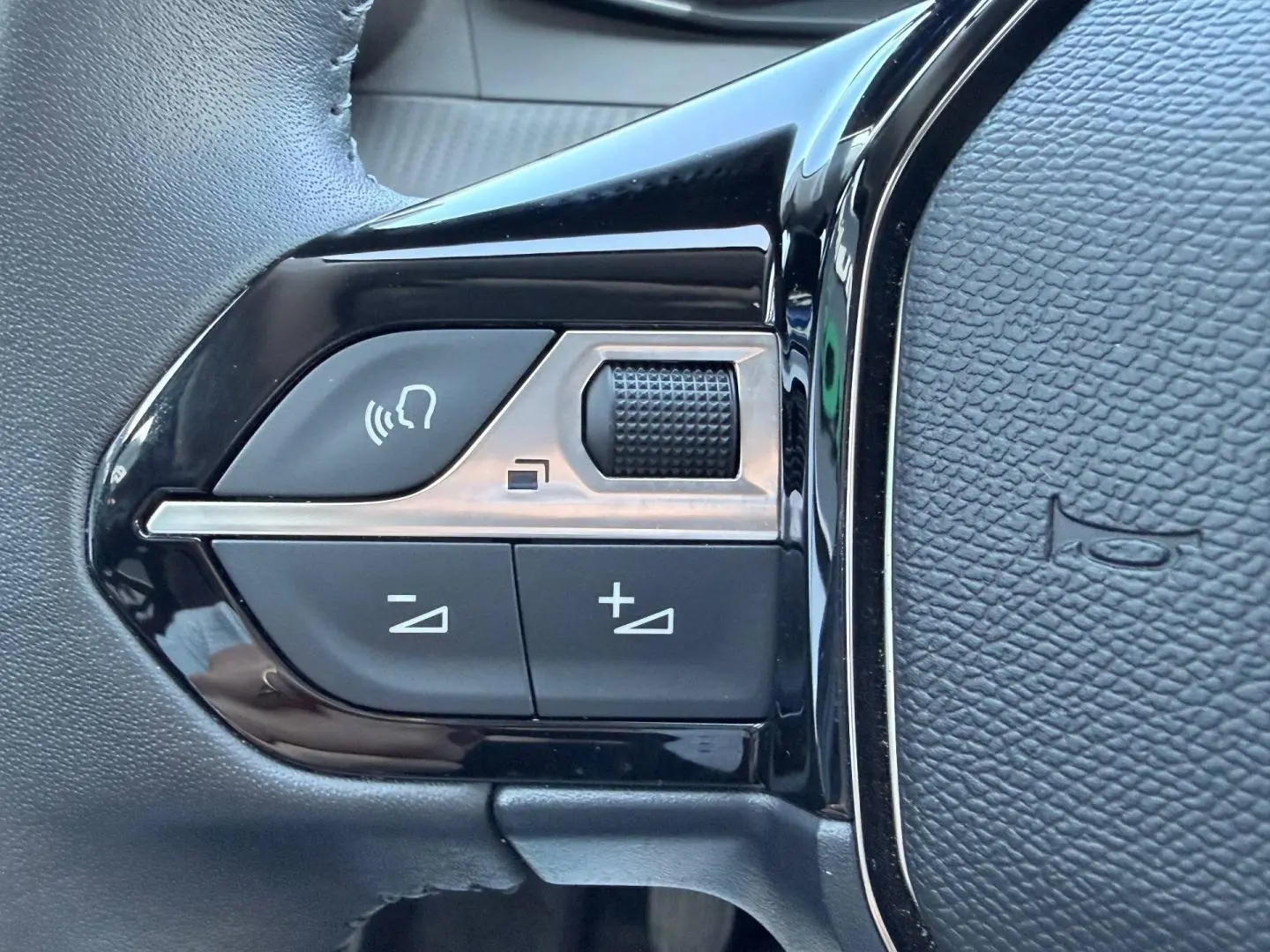 Gros plan sur les commandes noires du volant de la Peugeot 208 1.2 100ch S&S Allure, finition Gris Artense.