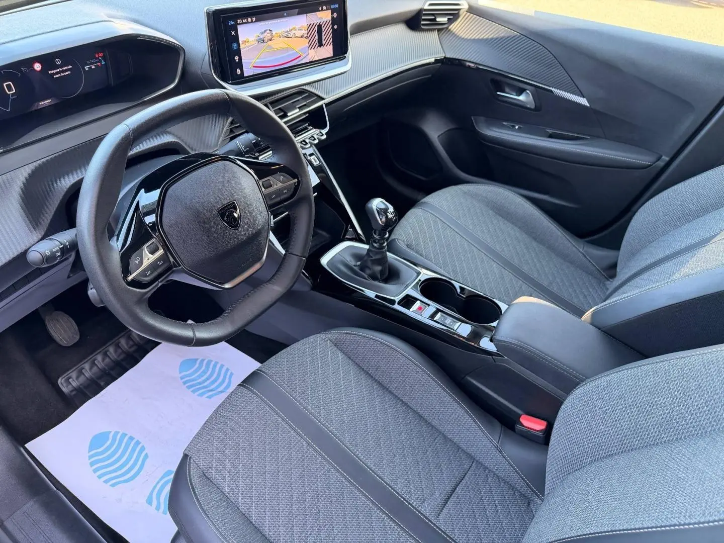 Vue intérieure côté conducteur de la Peugeot 208 1.2 100ch gris Artense, volant compact et écran tactile central visible.