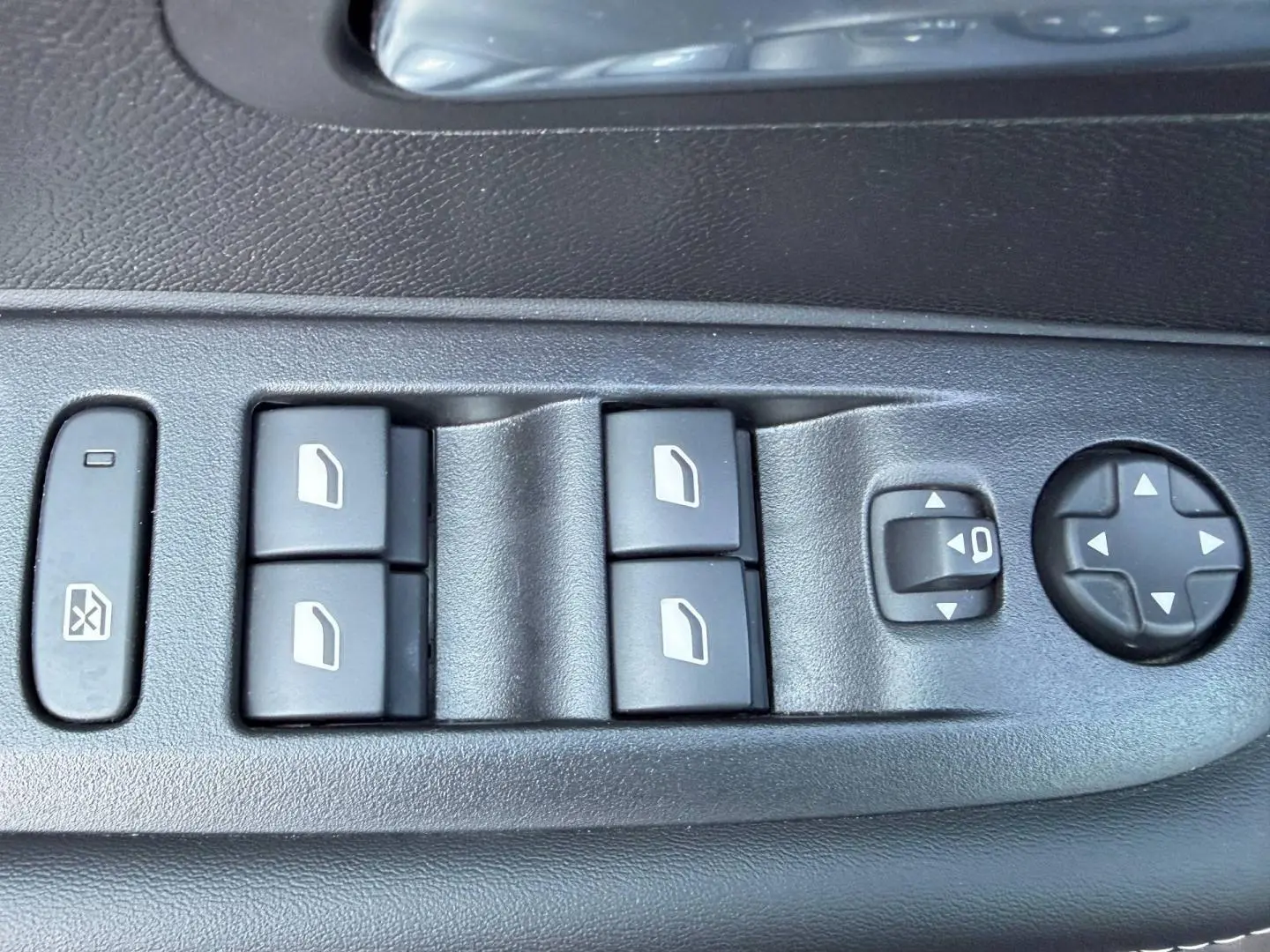 Gros plan sur les commandes de lève-vitres et réglage des rétroviseurs côté conducteur dans l’habitacle noir du Peugeot 208 gris Artense.