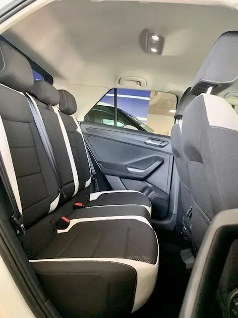Vue intérieure arrière côté droit du Volkswagen T-Roc blanc 2021, sièges noirs avec surpiqûres claires et ceinture blanche.
