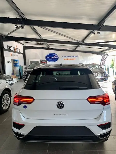 Vue arrière d'un Volkswagen T-Roc blanc 2021 en showroom, avec feux LED allumés et toit noir contrastant.