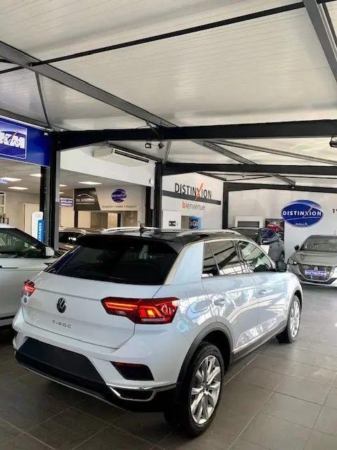Volkswagen T-Roc blanc en 3/4 arrière droit dans un showroom avec feux arrière LED allumés et toit noir.