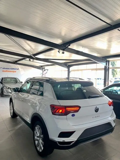 Vue 3/4 arrière droite d'un Volkswagen T-Roc blanc 2021 en showroom avec feux arrière allumés.