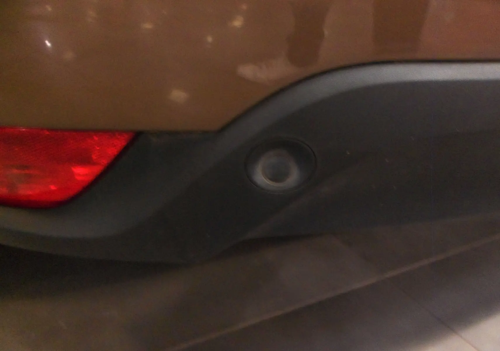 Gros plan sur le capteur de recul arrière intégré dans le pare-chocs noir d'une Renault Mégane IV brun cappuccino.