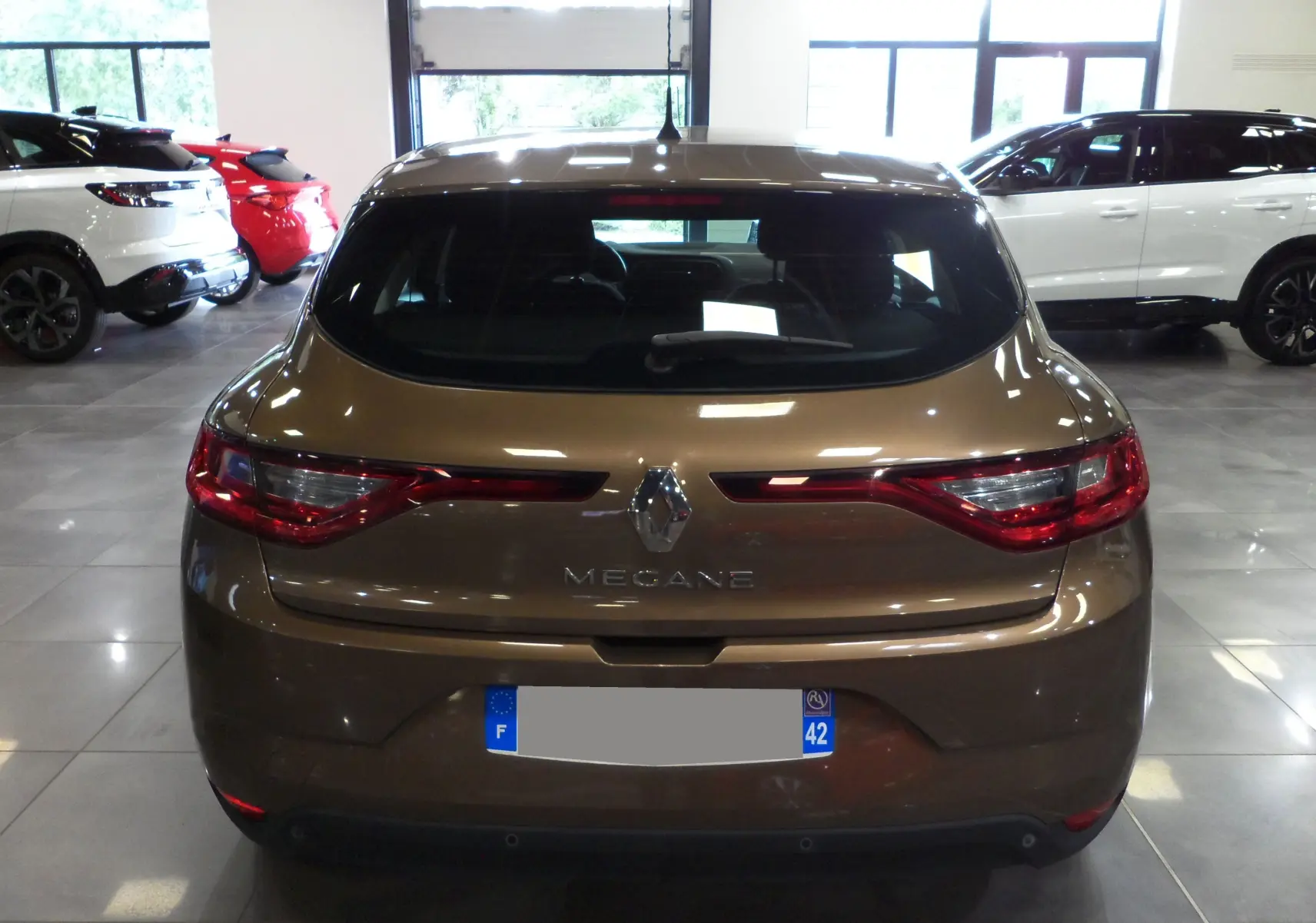 Vue arrière d'une Renault Mégane IV TCe 100 Life brun cappuccino dans un showroom lumineux.