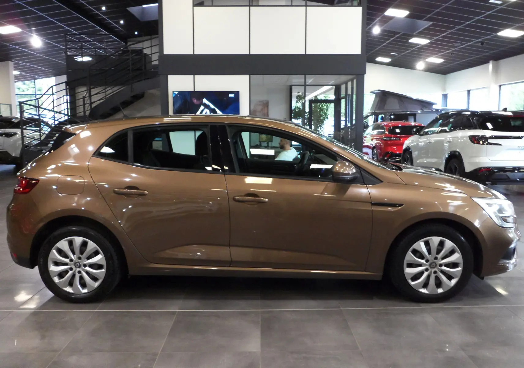 Profil côté droit d'une Renault Mégane IV TCe 100 Life brun cappuccino dans un showroom lumineux.