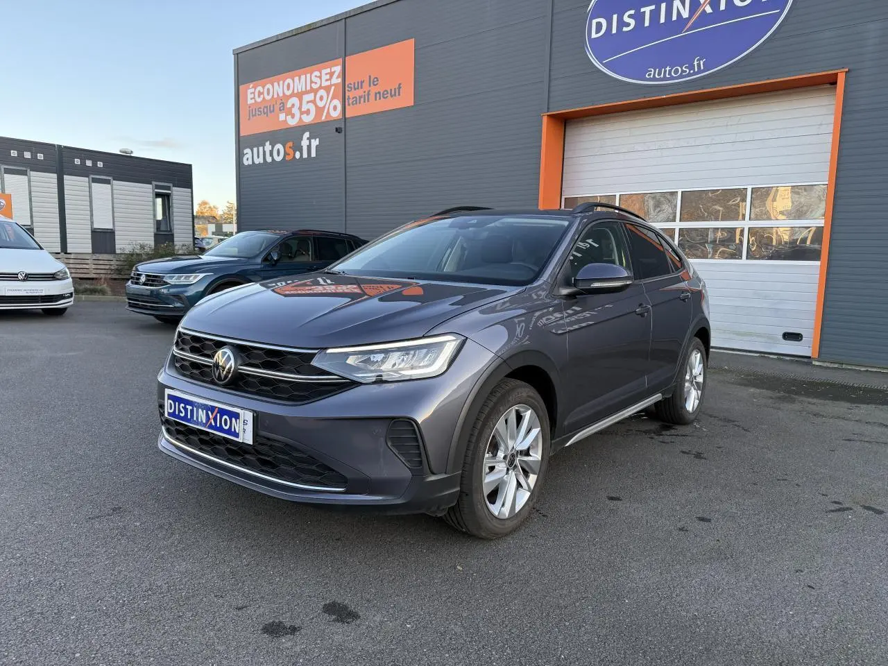 Volkswagen Taigo 2025 gris INC en 3/4 avant droit, avec jantes alliage et toit noir visible devant un bâtiment commercial.