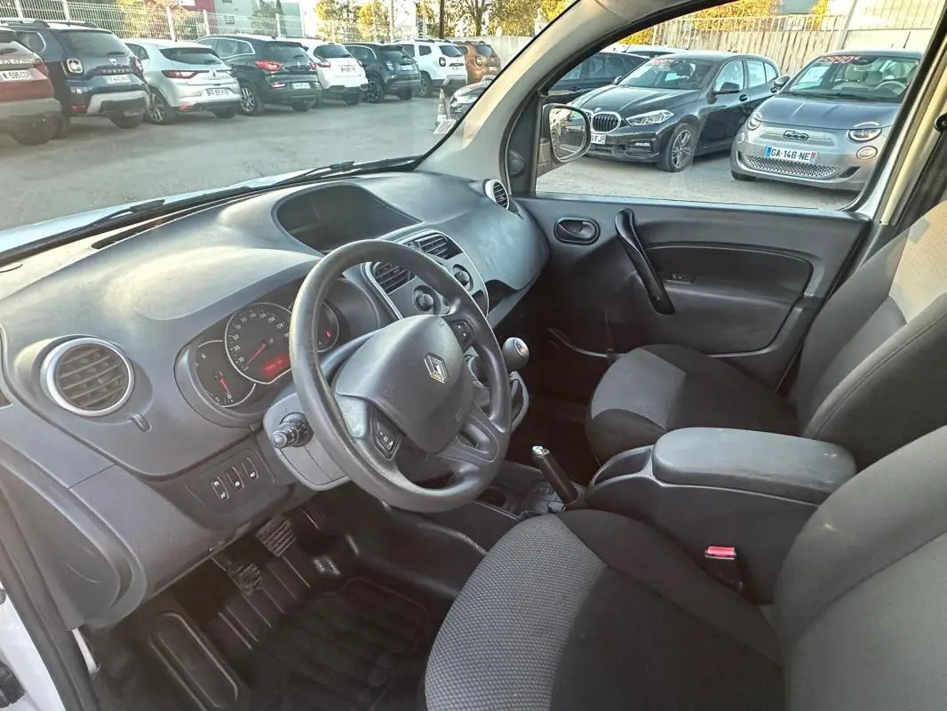 Vue intérieure côté conducteur du Renault Kangoo Express blanc, montrant le tableau de bord et les sièges noirs.