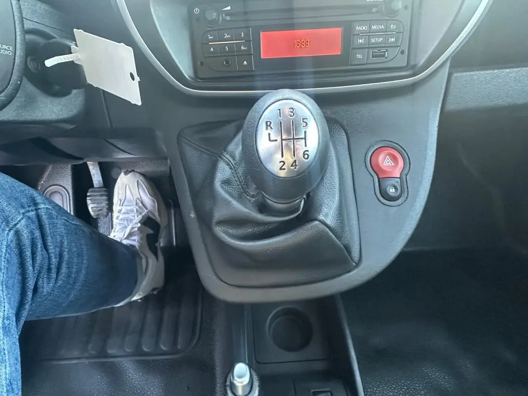 Gros plan sur le levier de vitesses manuelle à six rapports du Renault Kangoo Express blanc, avec tableau de bord et pédales visibles.