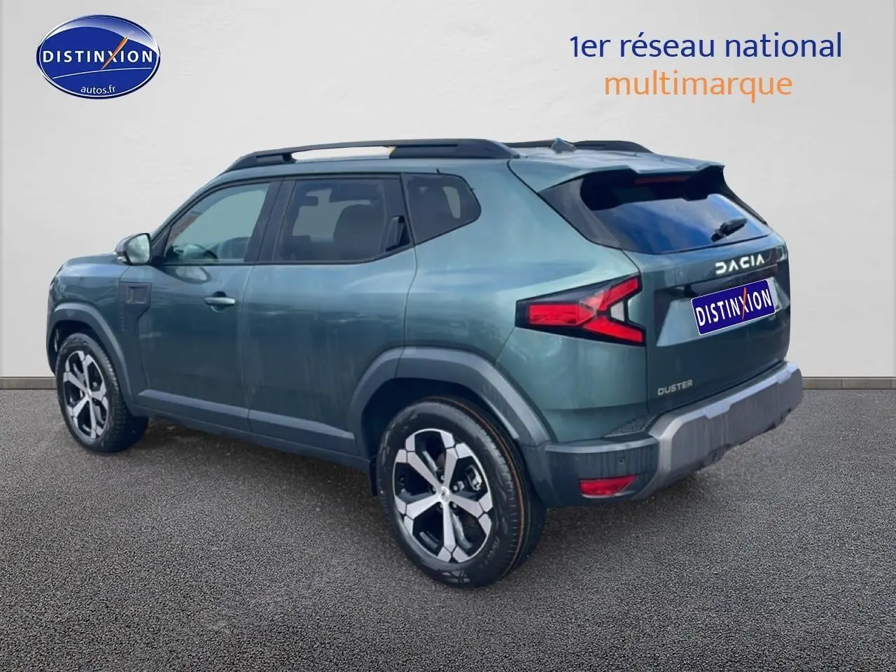 Vue 3/4 arrière droite du Dacia Duster 2026 vert cèdre avec barres de toit et jantes alu distinctives.