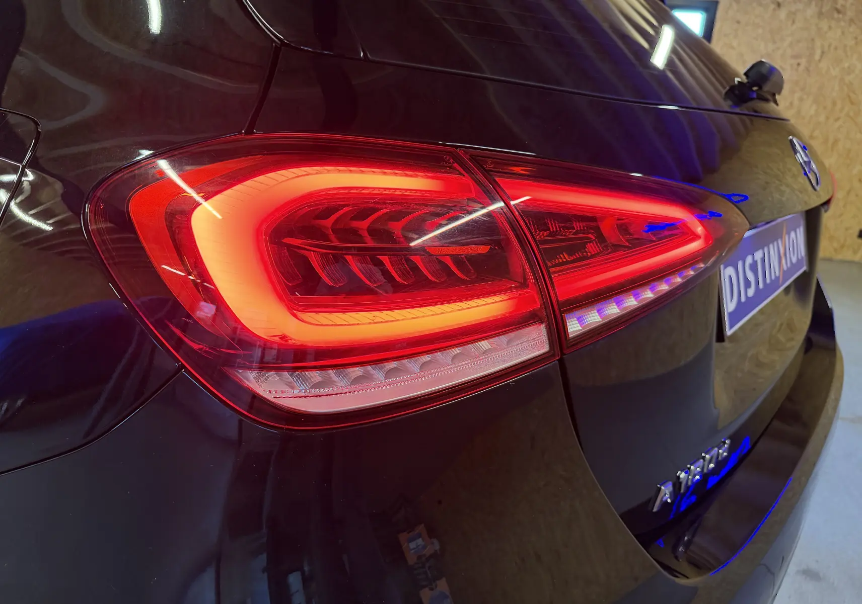 Gros plan sur le feu arrière droit rouge d'une Mercedes Classe A noire, avec reflet et logo visible sur le hayon.