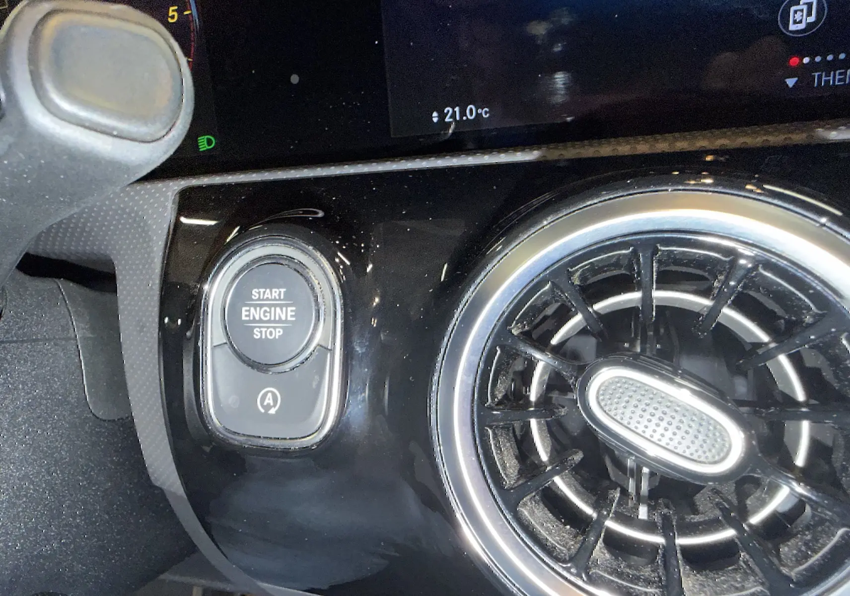 Détail intérieur montrant le bouton Start/Stop et la sortie d'air ronde chromée d'une Mercedes Classe A noire.