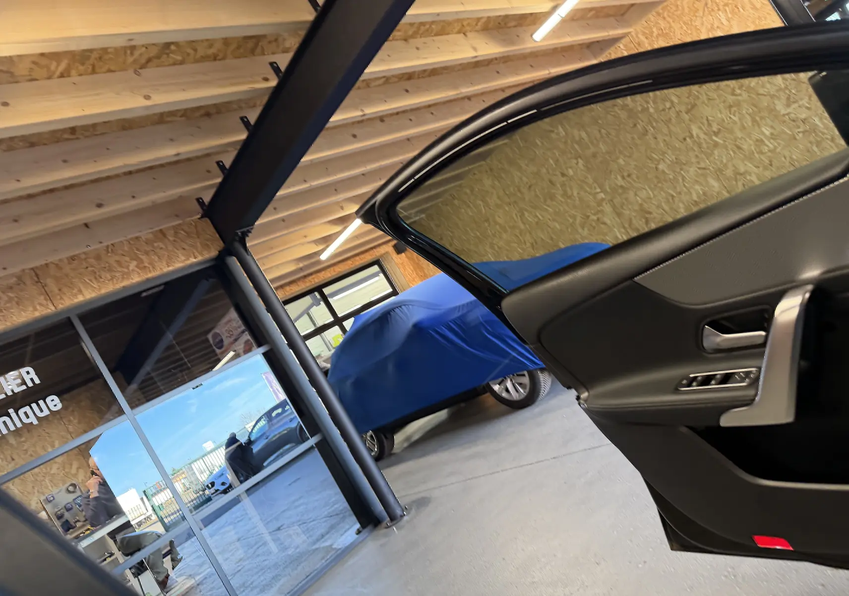 Vue intérieure côté droit de la porte ouverte d’une Mercedes Classe A noire, avec un véhicule bleu couvert en arrière-plan.