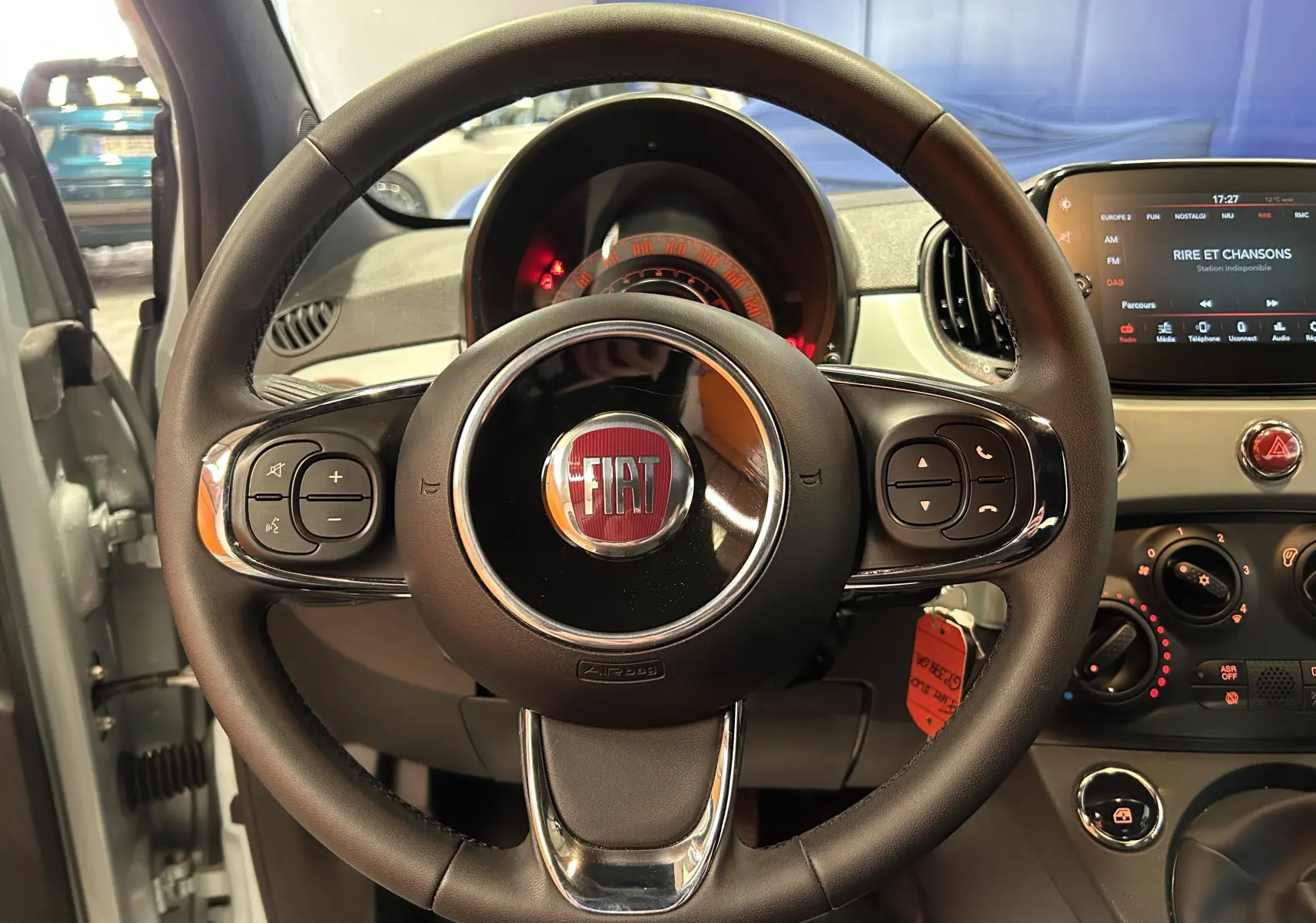 Vue intérieure centrée sur le volant noir du Fiat 500 2023 avec tableau de bord et écran tactile en arrière-plan.