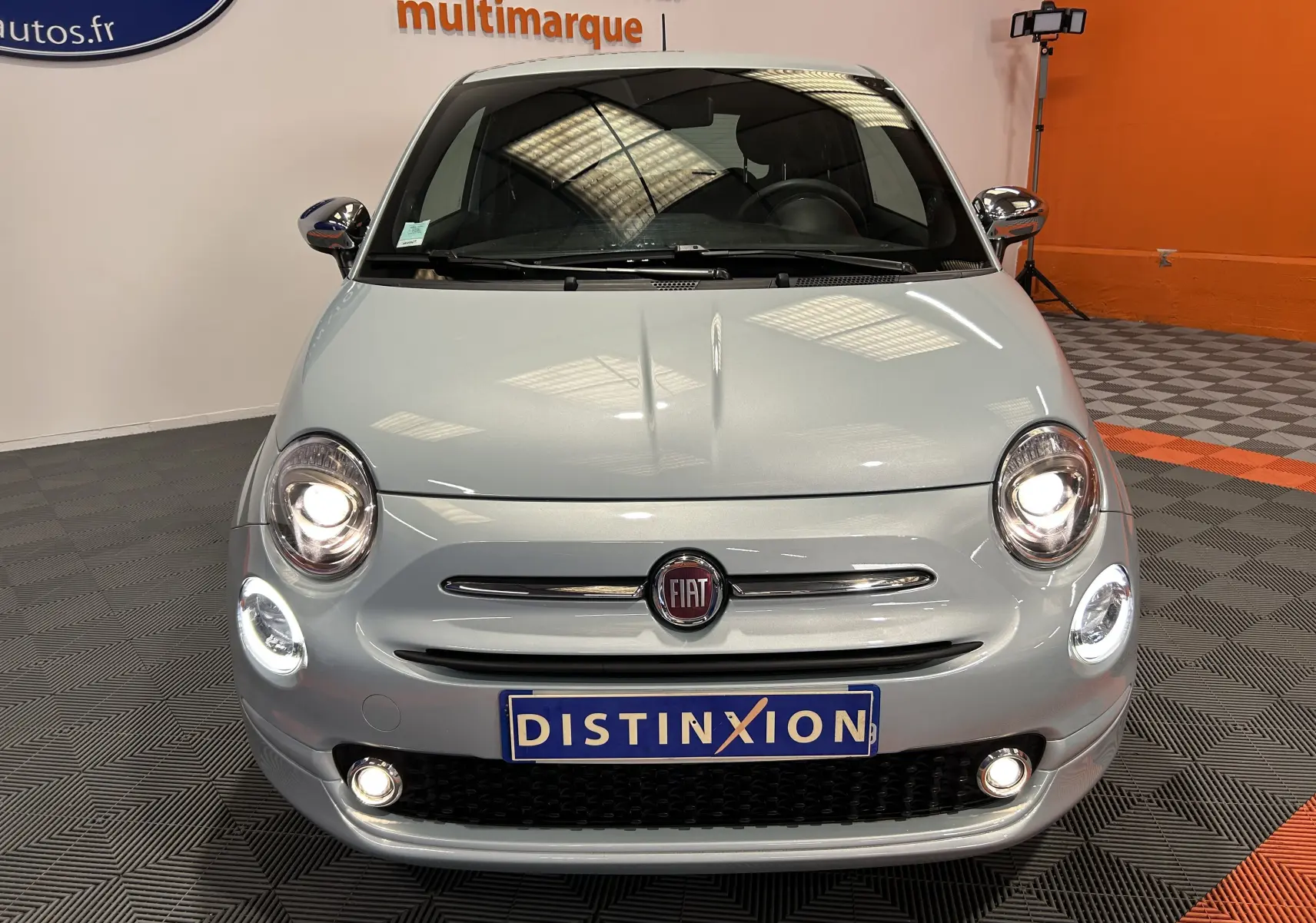Vue avant d'une FIAT 500 2023 en gris clair avec phares allumés et plaque d'immatriculation Distinxion visible.