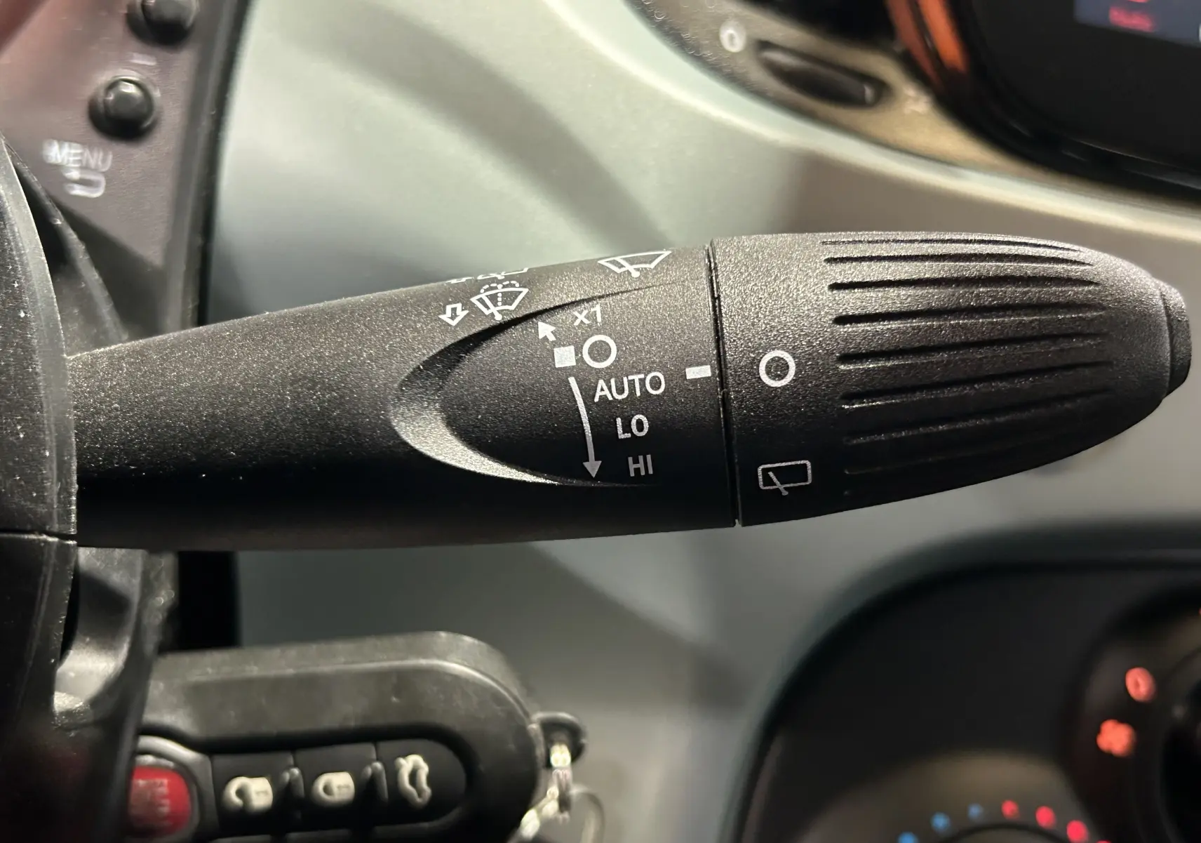 Gros plan sur la manette d’essuie-glace noire avec commandes blanches dans l’habitacle d’une FIAT 500 Rugiada Green 2023.