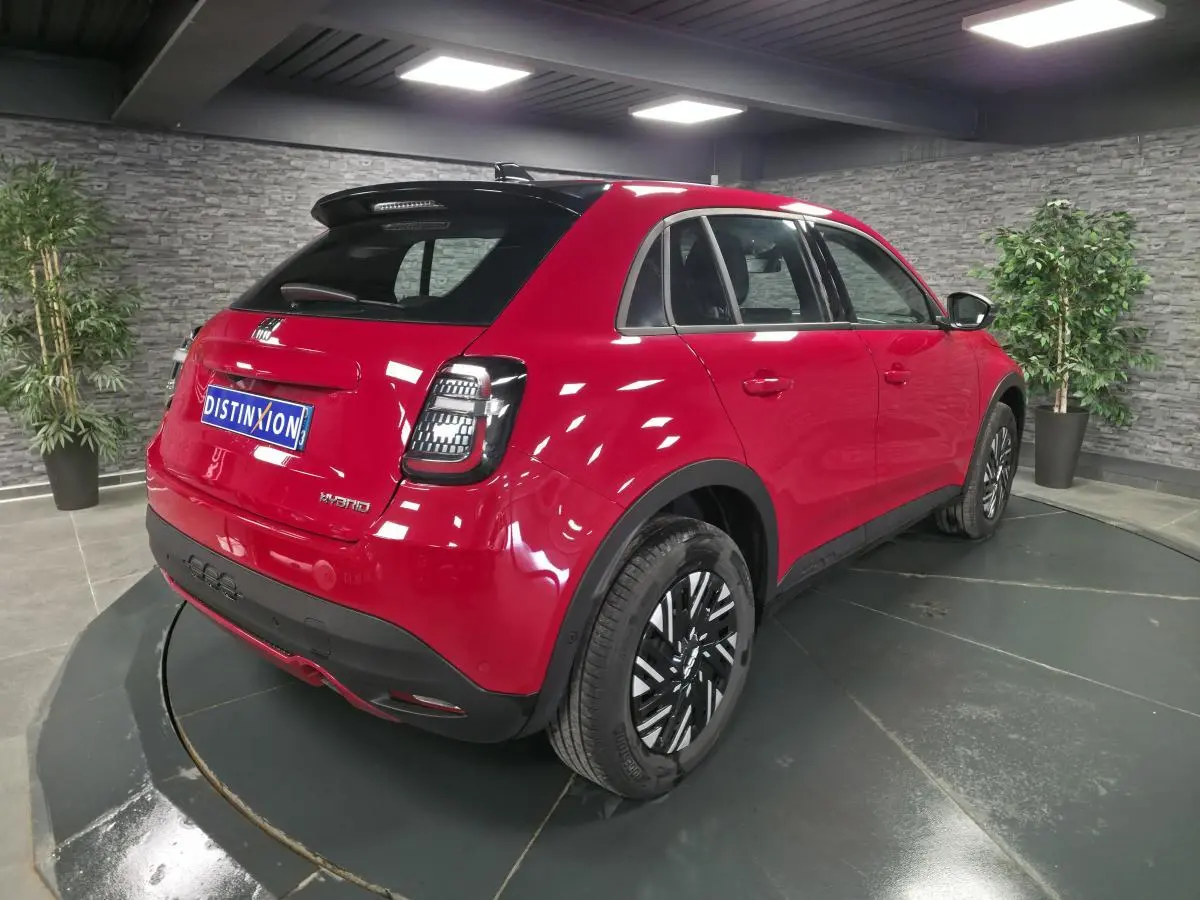 Vue 3/4 arrière droite d'une FIAT 600 rouge hybride 2024 avec jantes bicolores et toit noir brillant en showroom.