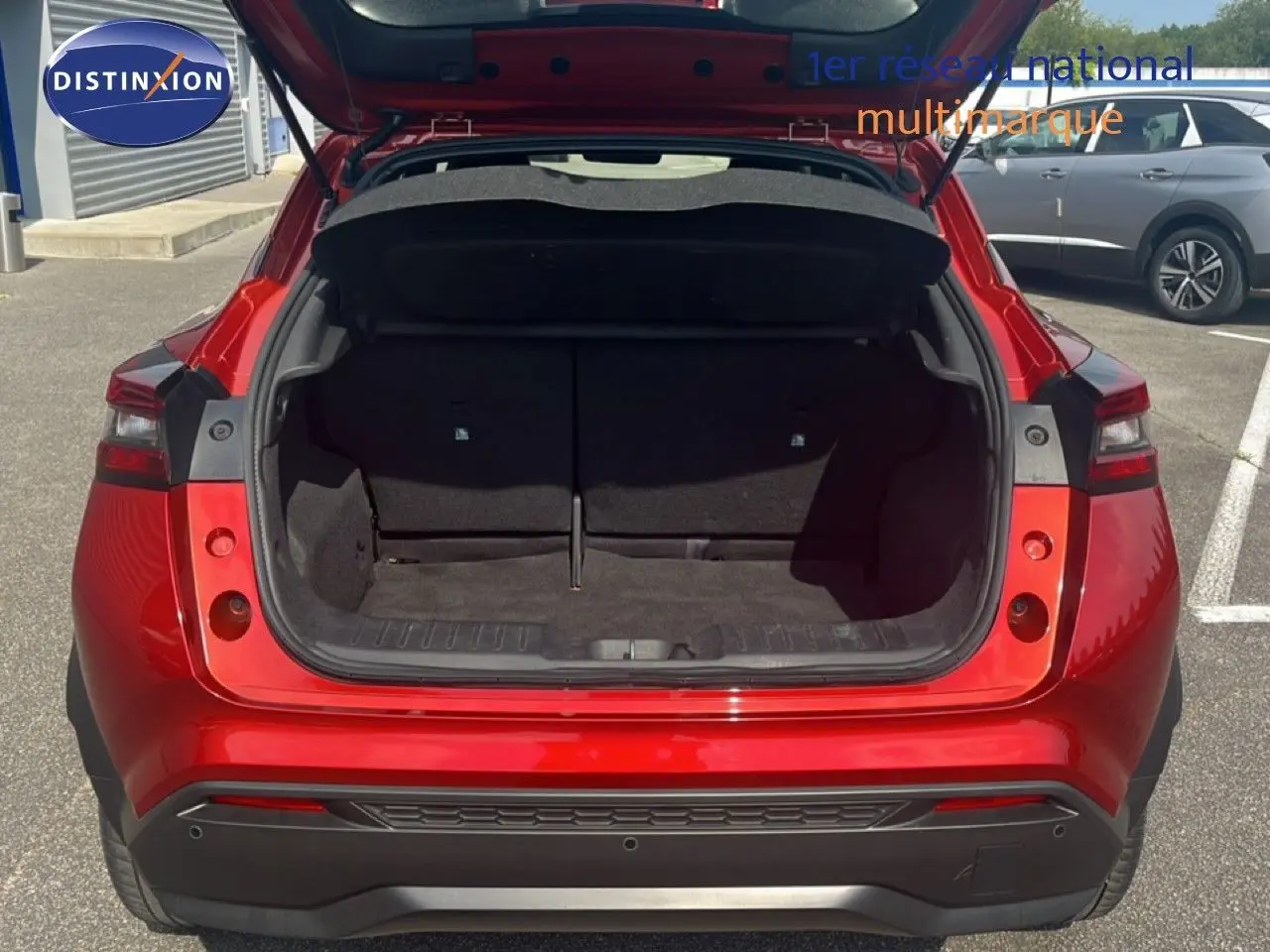 Vue arrière du Nissan Juke 2024 rouge Fuji Metal avec coffre ouvert, montrant l'espace de chargement vide.