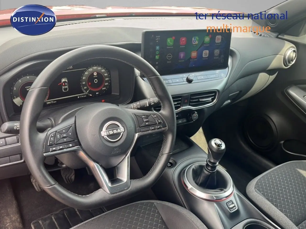 Vue intérieure du poste de conduite du Nissan Juke 2024, volant cuir et levier de vitesse manuel, écran tactile central visible.