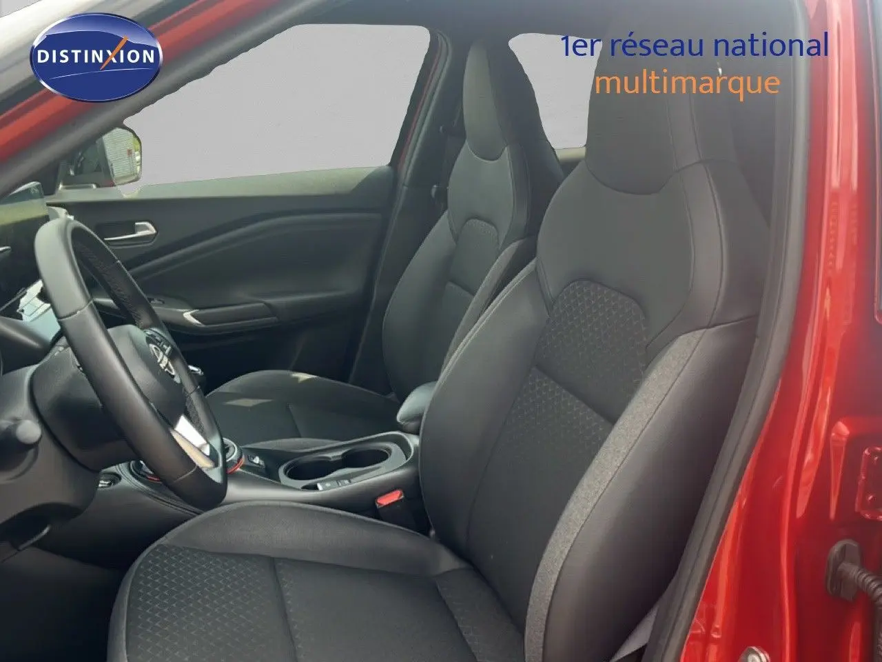 Vue intérieure côté conducteur du Nissan Juke 2024 rouge Fuji Metal, sièges tissu noir avec détails gris et volant multifonction.