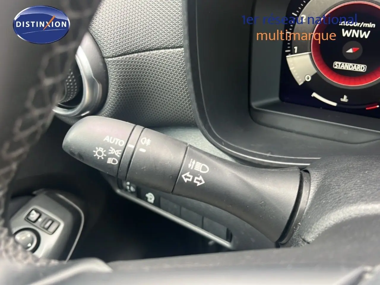 Gros plan sur la commande des phares et clignotants du tableau de bord d’un Nissan Juke rouge Fuji Metal 2024.
