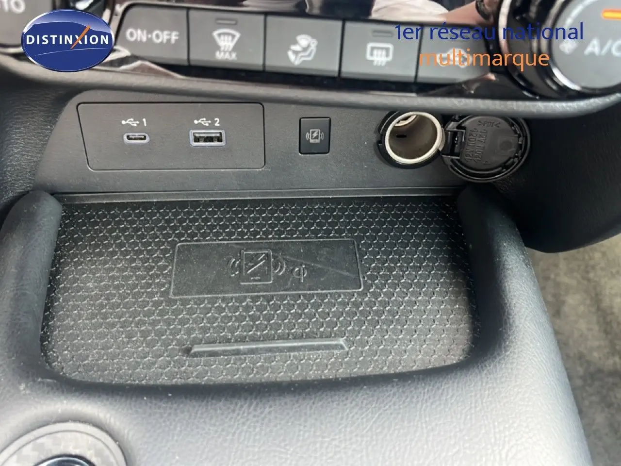 Vue rapprochée de la console centrale du Nissan Juke rouge Fuji Metal 2024, montrant ports USB, prise 12V et zone de recharge sans fil.
