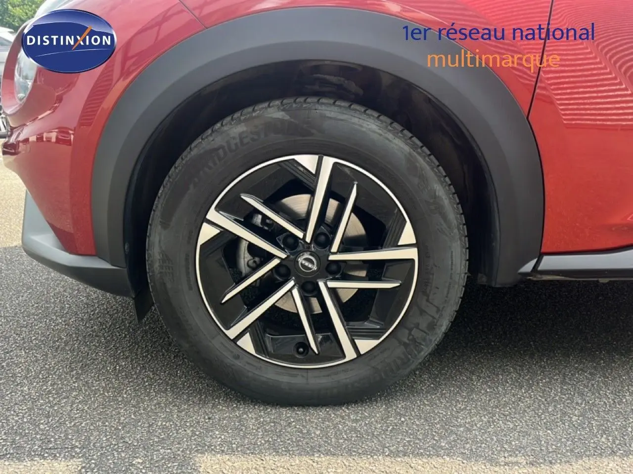 Gros plan sur la roue avant gauche du Nissan Juke rouge Fuji Metal avec jante alliage noire et argentée.