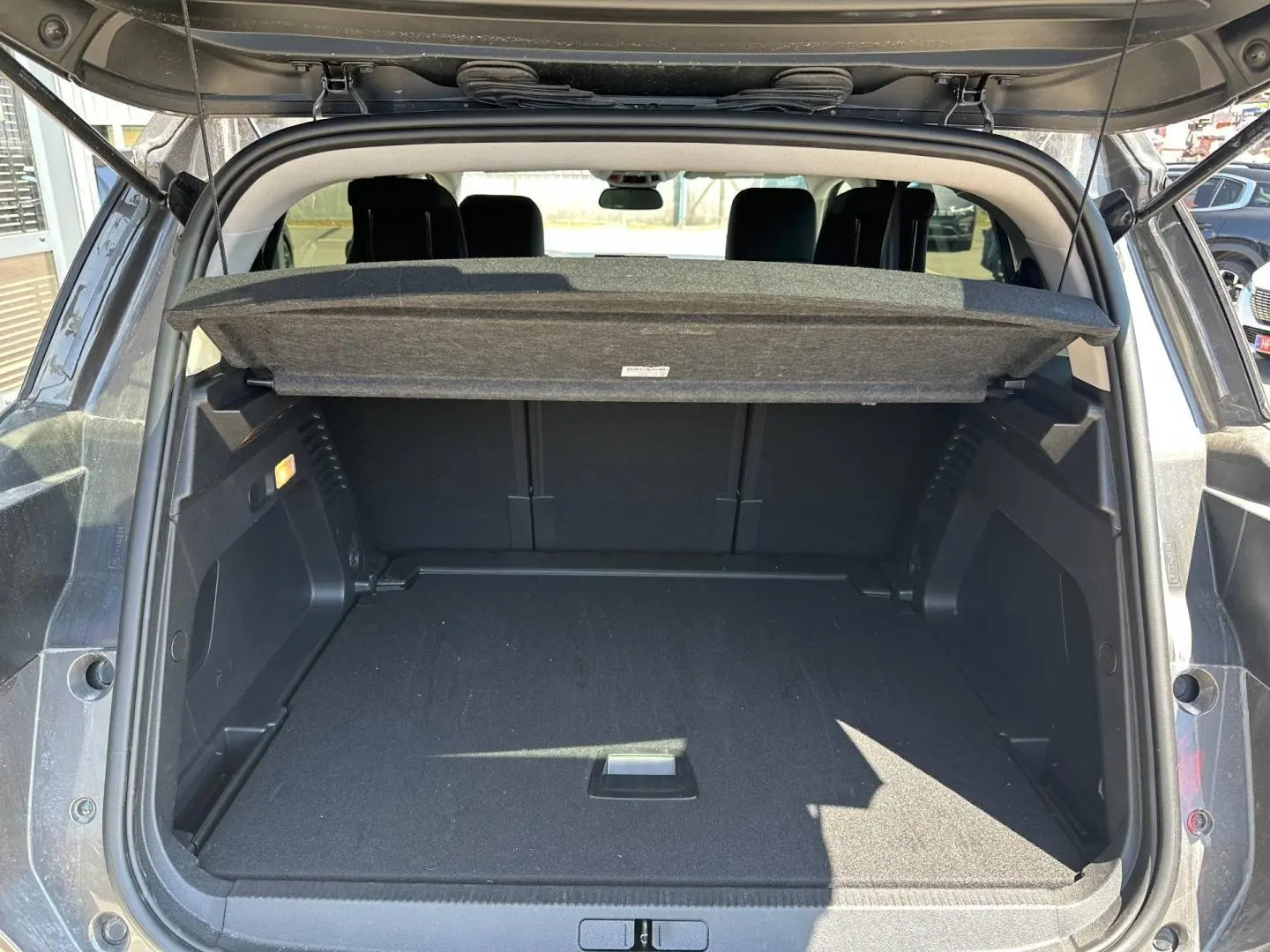 Coffre ouvert vu de l'arrière d'un Citroën C5 Aircross gris Platinium avec cache-bagages relevé.