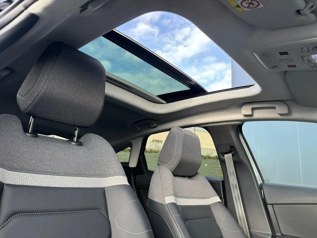 Vue intérieure avant des sièges gris chiné avec toit ouvrant panoramique ouvert sur ciel bleu.