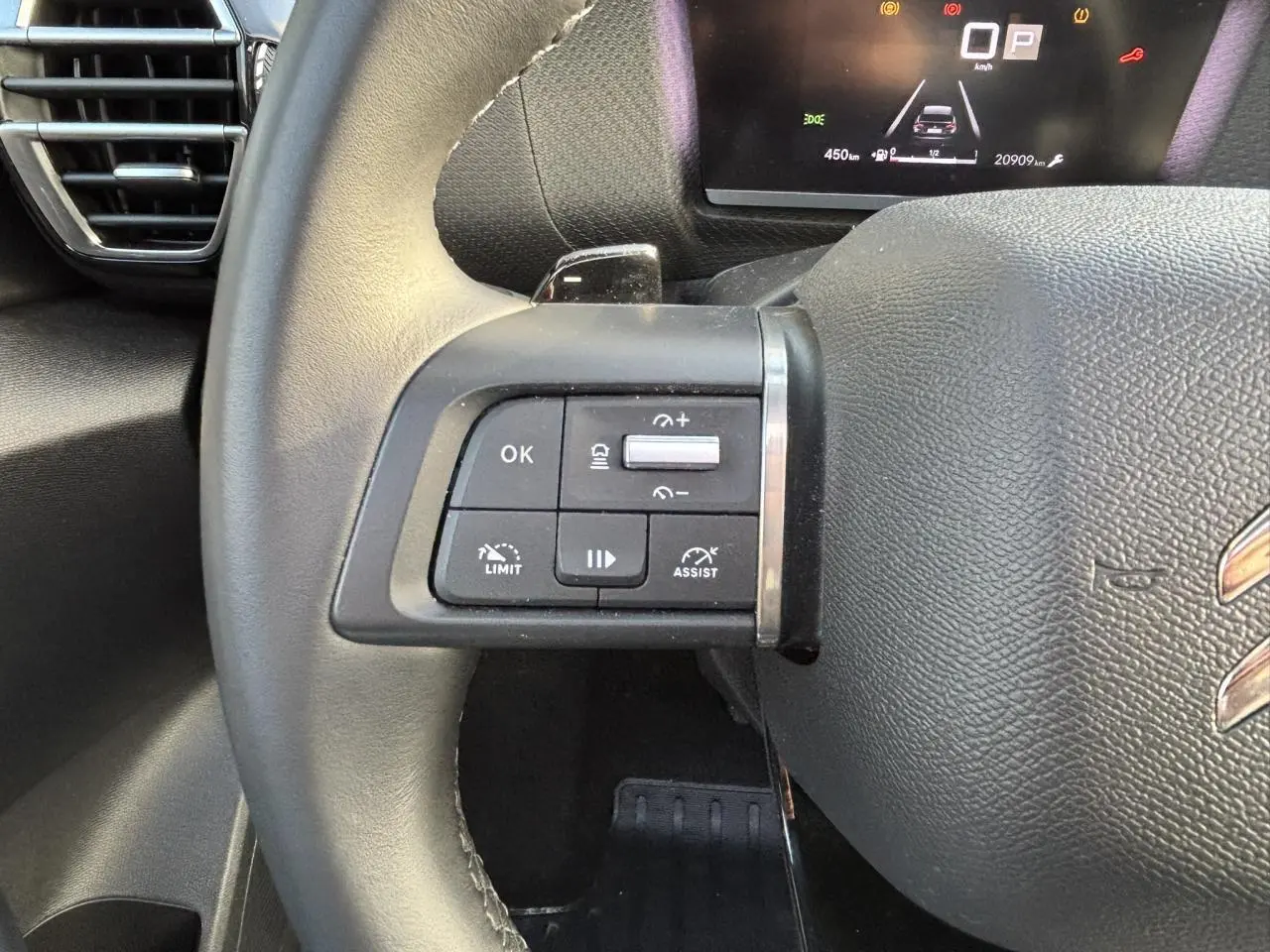 Gros plan sur les commandes au volant gauche en cuir noir du Citroën C4 2024 avec affichage numérique en arrière-plan.