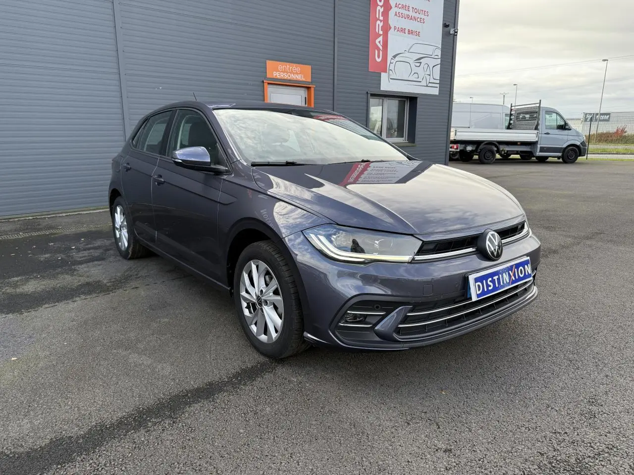 Volkswagen Polo gris cendre vue 3/4 avant droit, avec jantes alliage et feux LED allumés.