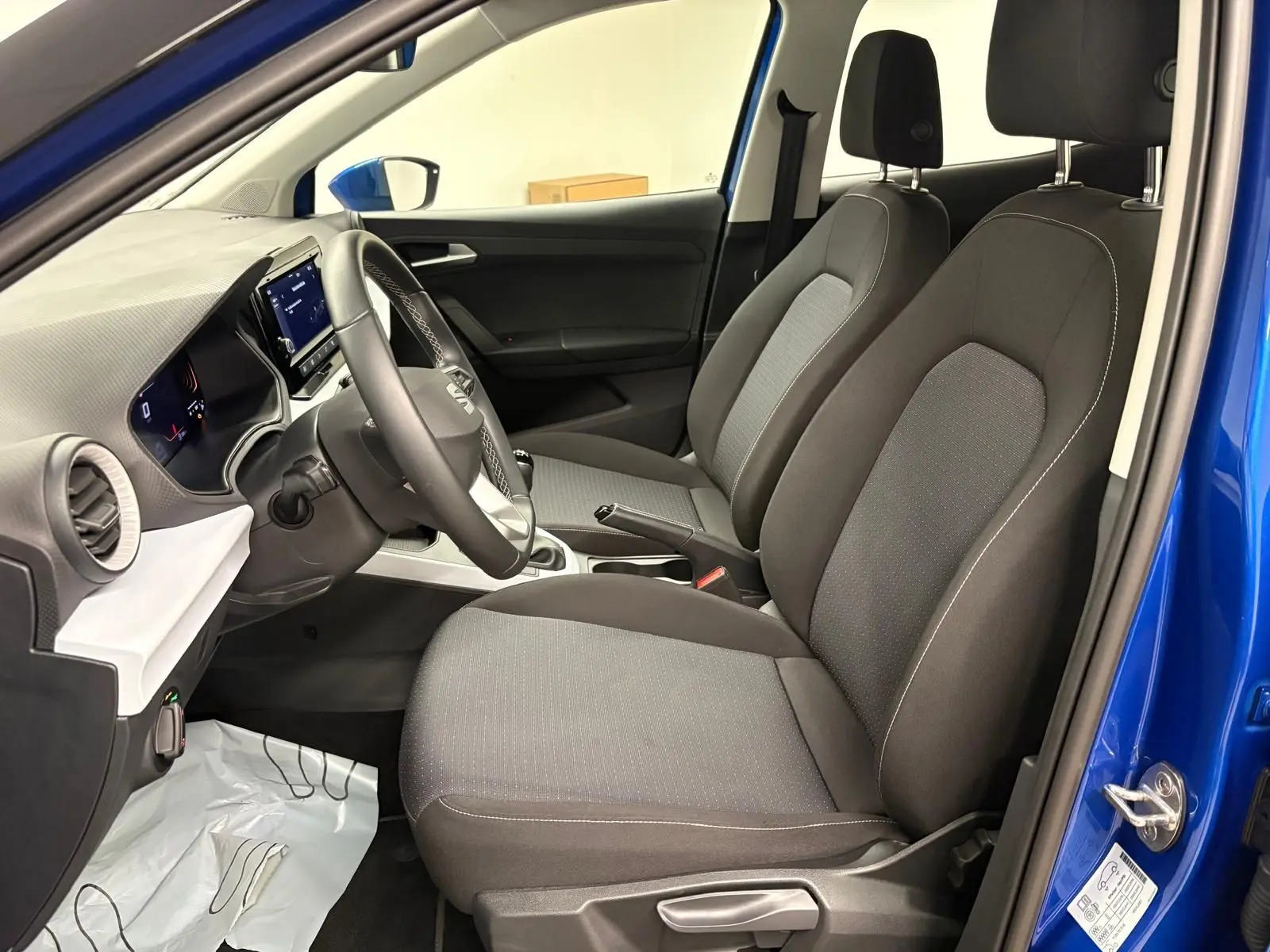 Vue intérieure côté conducteur du SEAT Arona 2025 bleu saphir, montrant les sièges avant et le tableau de bord.