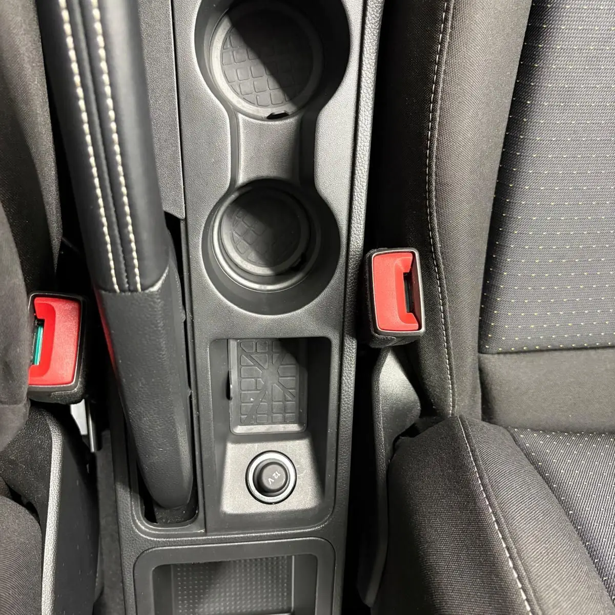 Gros plan sur la console centrale intérieure du SEAT Arona 2025, avec porte-gobelets, frein à main et bouton 12V.