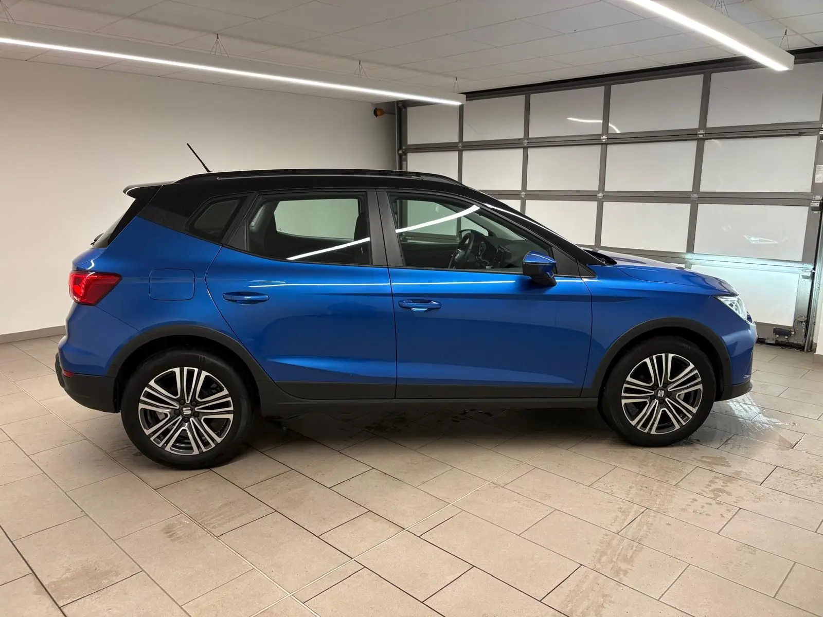 Vue de profil côté gauche d'un SEAT Arona 2025 bleu saphir avec toit noir, roues alliage et détails noirs contrastants.