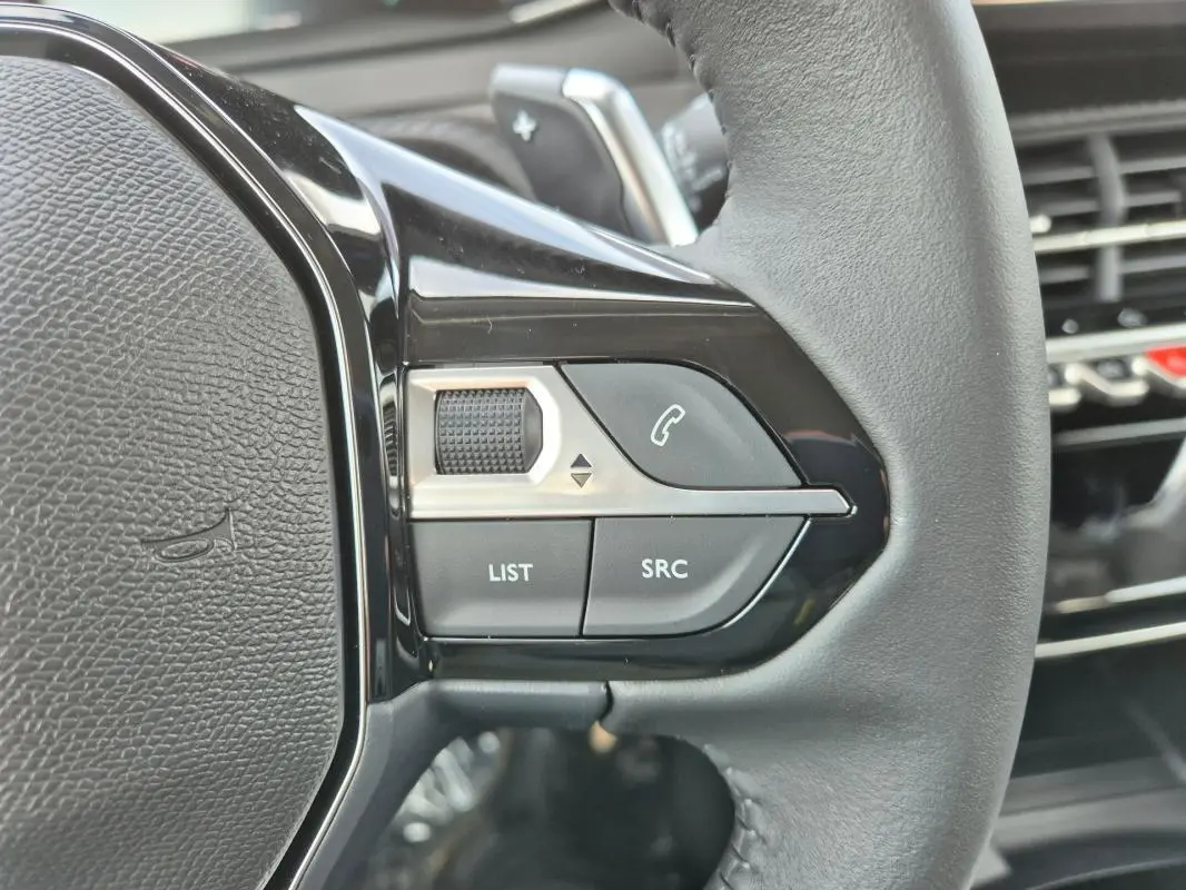 Gros plan sur les commandes gauche du volant cuir d’une Peugeot 208 blanche, avec boutons de téléphone et réglages audio.