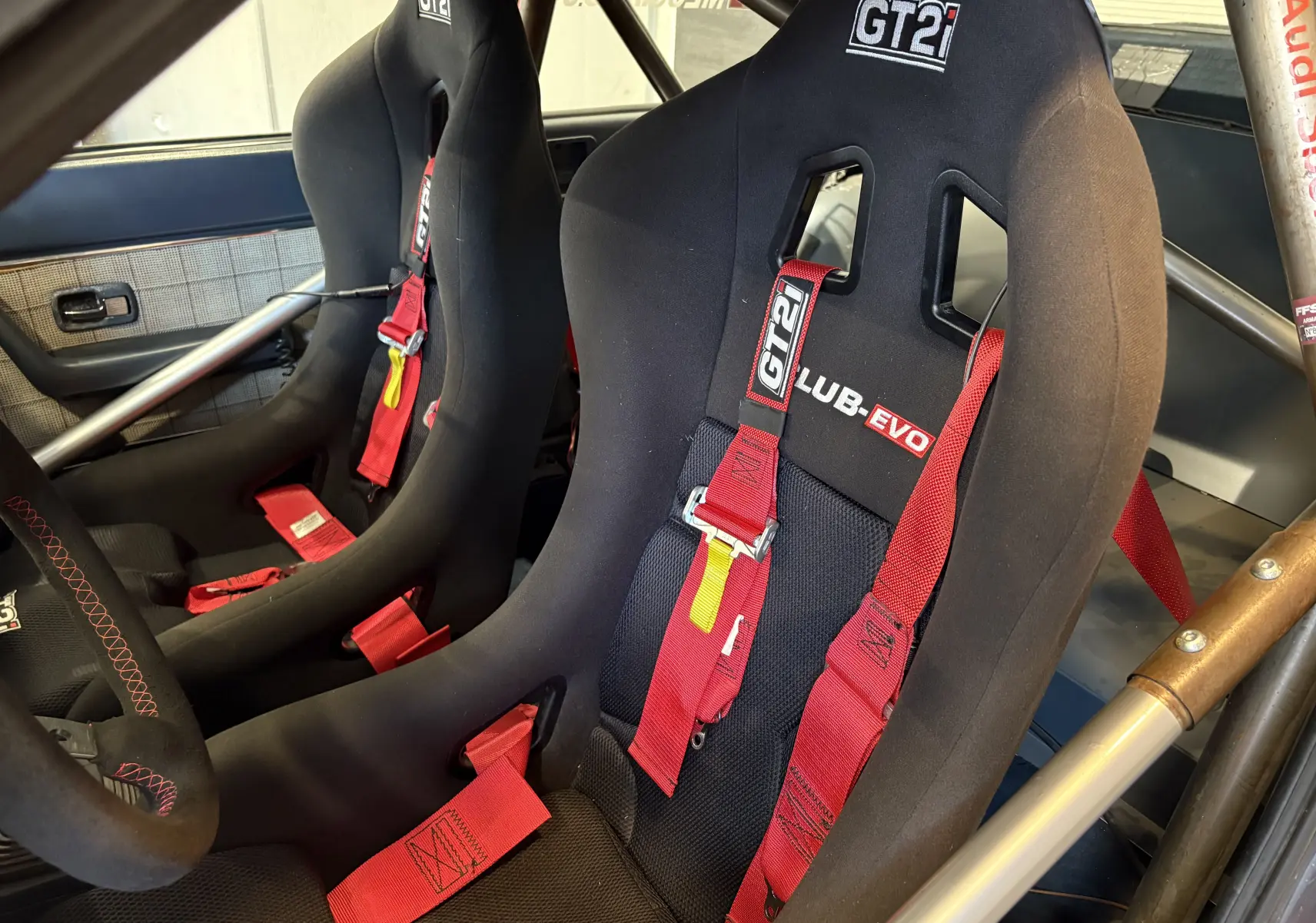 Gros plan intérieur sur les sièges baquets noirs GT2i avec harnais rouges dans un Audi Coupé GT noir de 1983 équipé pour rallye.