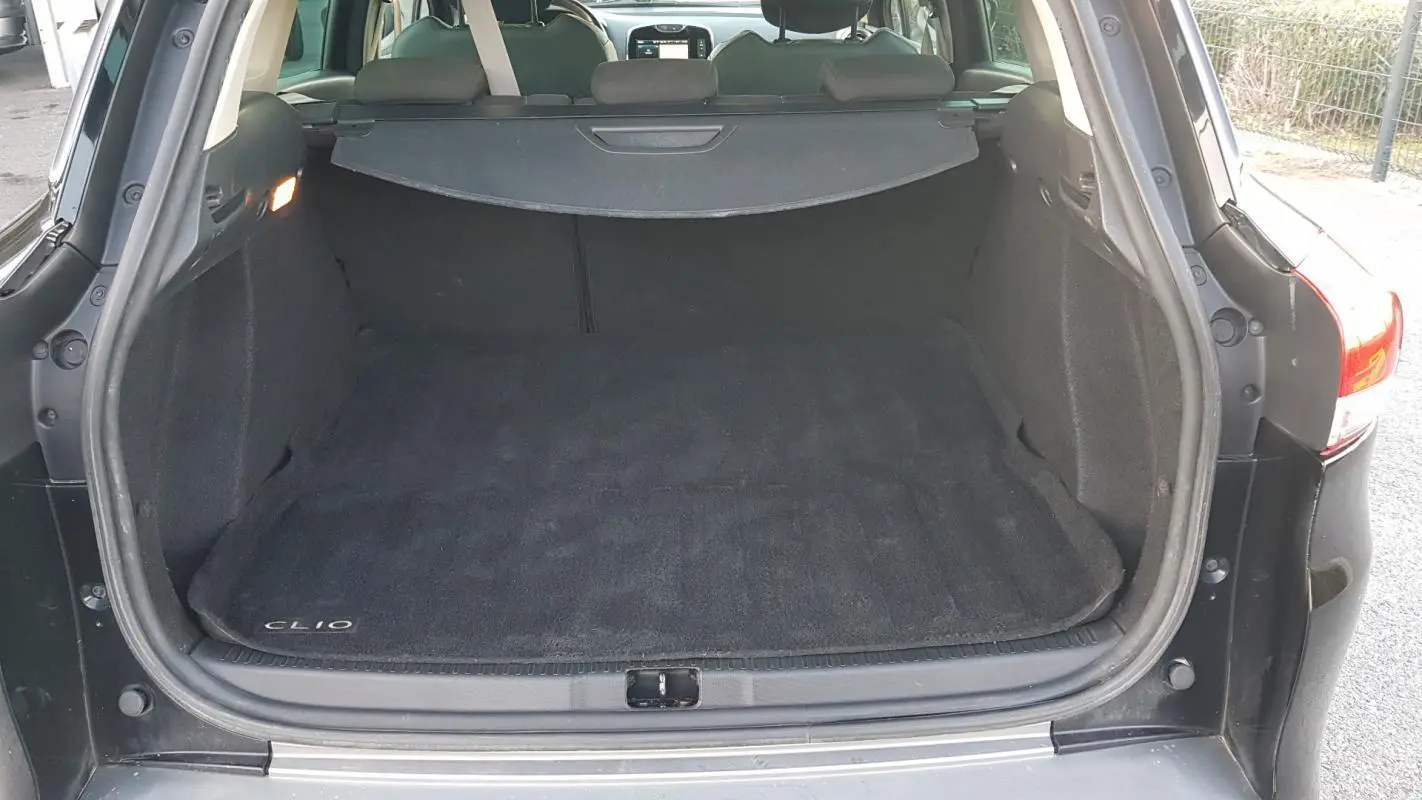 Coffre ouvert d'une Renault Clio IV Estate noire, vue arrière montrant l'espace de chargement avec tapis marqué Clio.