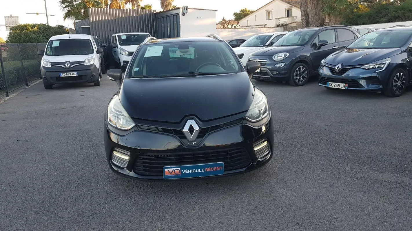 Vue de face d'une Renault Clio IV Estate noire avec feux diurnes allumés sur un parking.