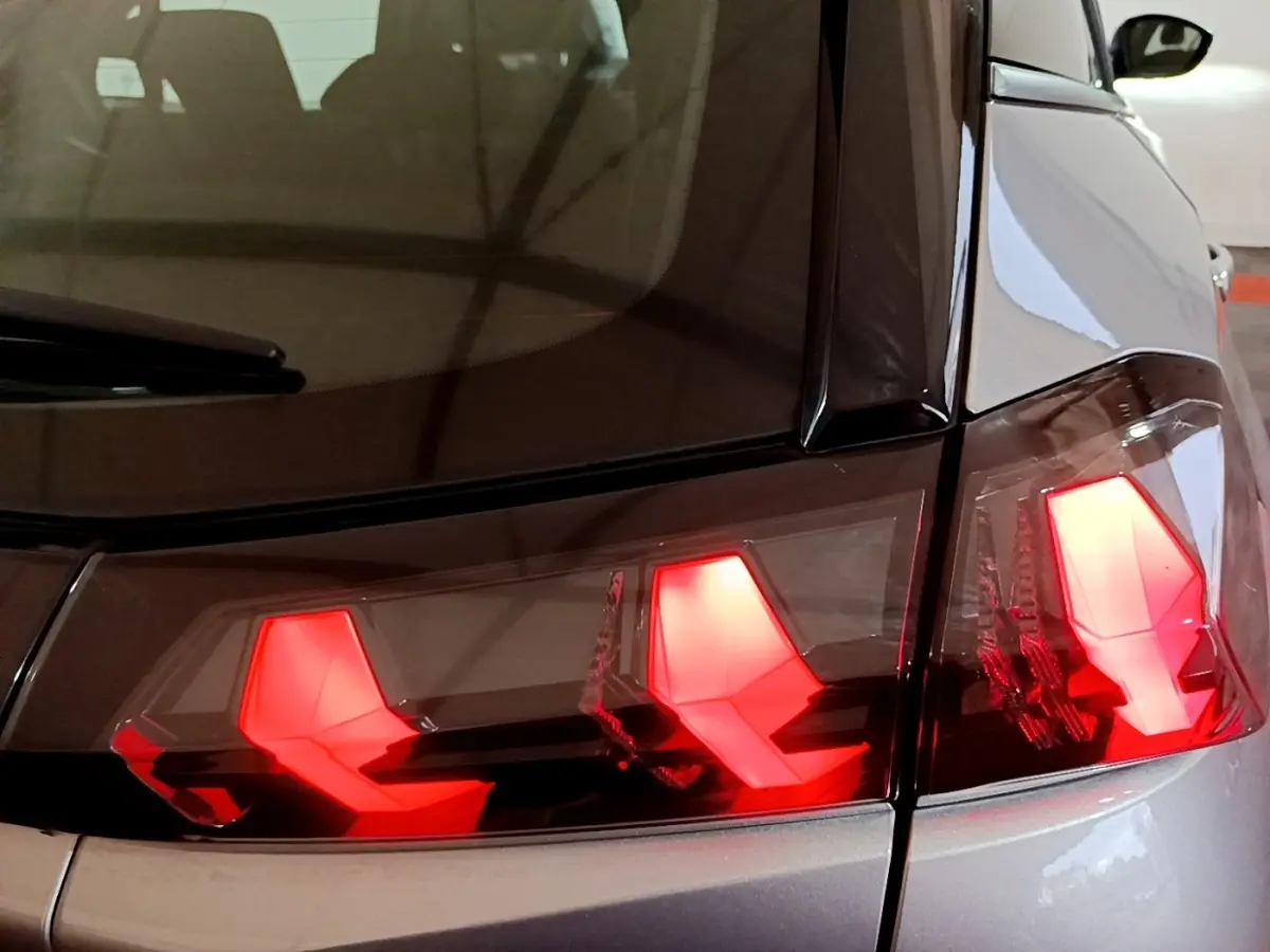 Gros plan sur les feux arrière allumés du côté gauche d’un Peugeot 2008 gris clair, vue arrière rapprochée.