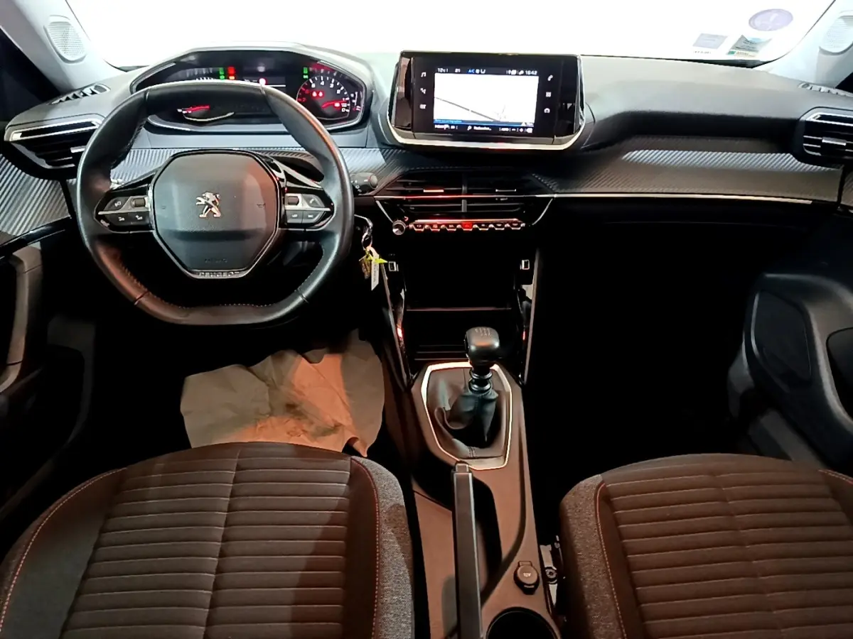 Vue intérieure avant du Peugeot 2008 gris clair 2021, volant cuir, écran tactile central et levier de vitesse manuel.