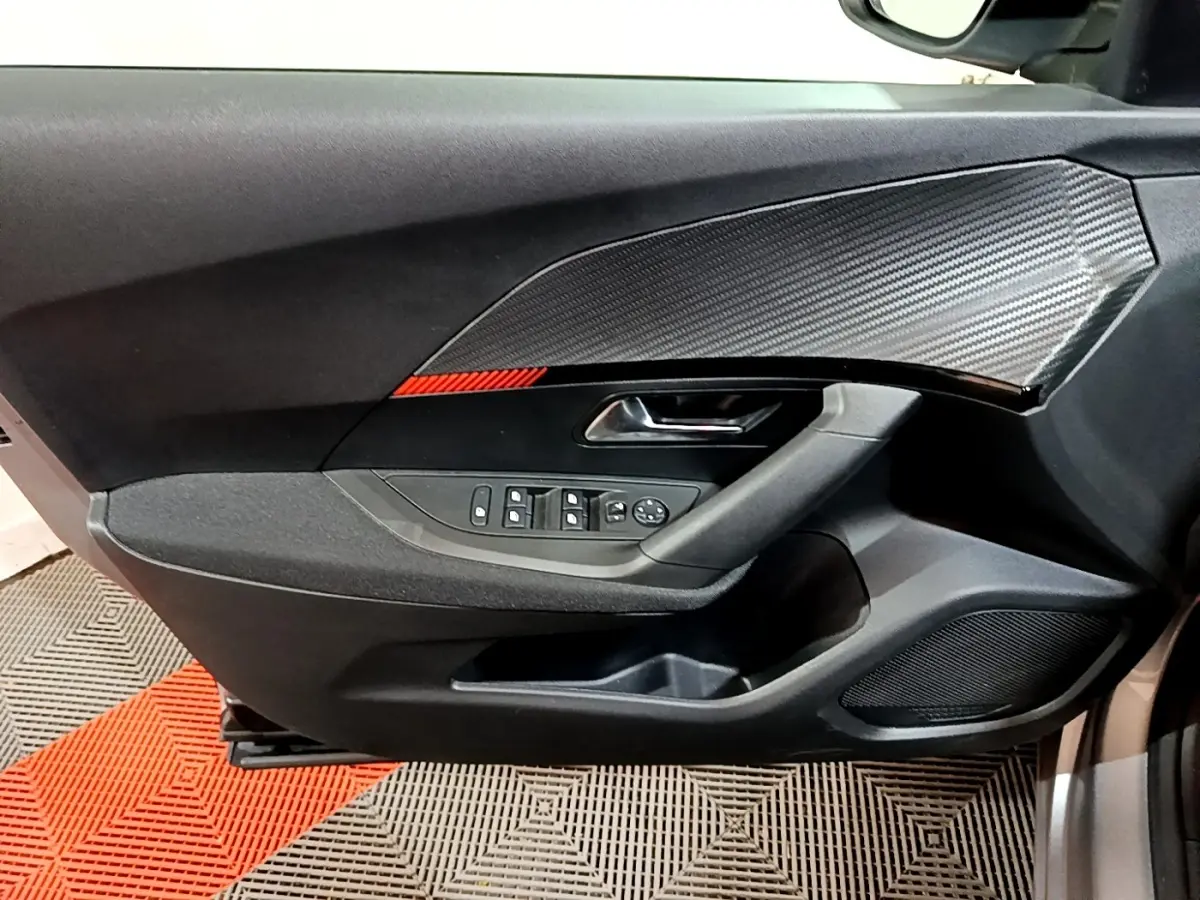 Vue intérieure côté gauche de la porte avant gris clair du Peugeot 2008 avec insert effet carbone et bande rouge décorative.