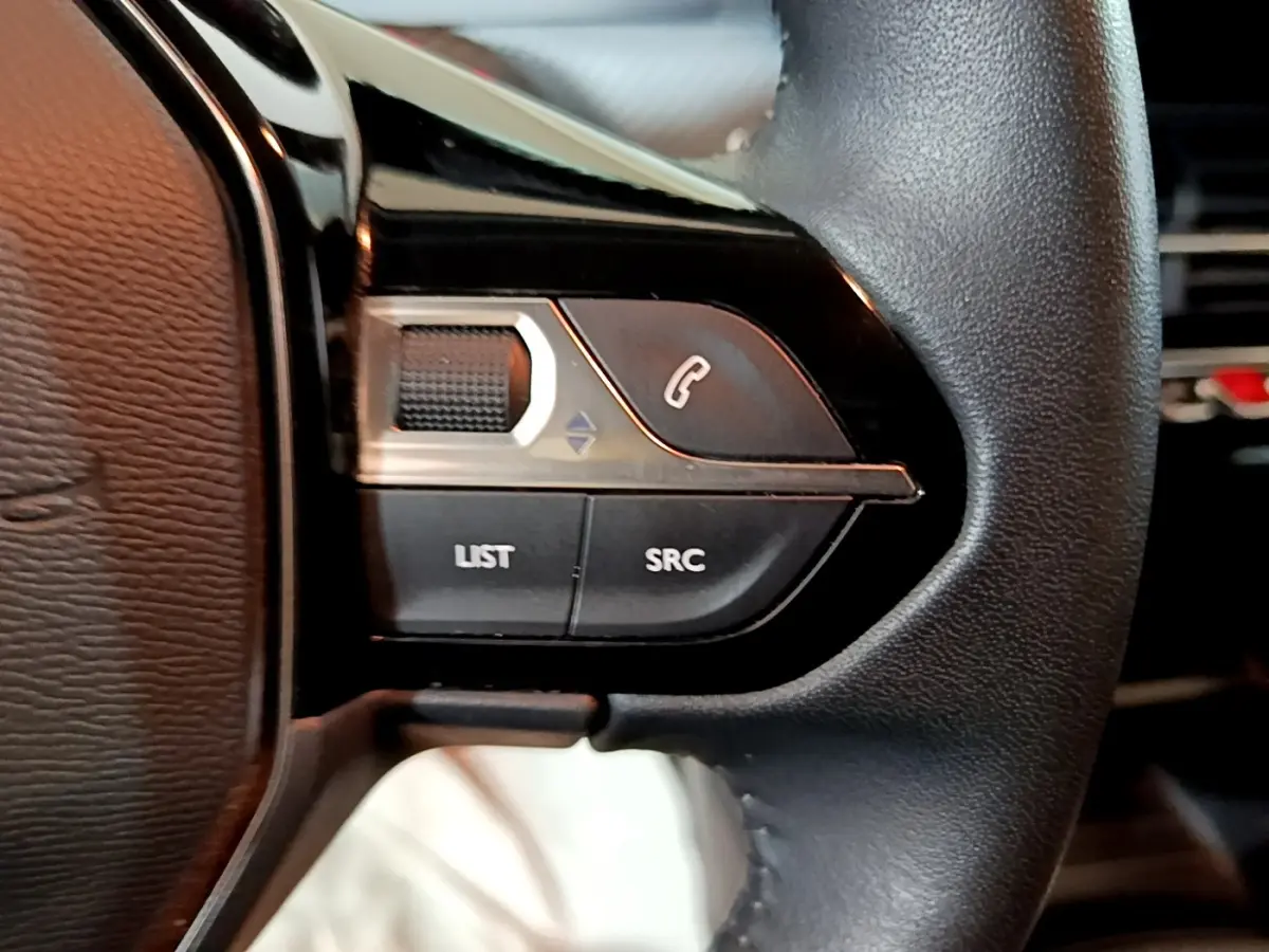 Gros plan sur les commandes gauche du volant cuir noir du Peugeot 2008 gris clair, avec boutons de téléphone et volume.