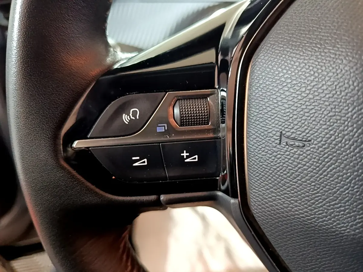 Gros plan sur les commandes vocales et volume au volant cuir côté gauche d’un Peugeot 2008 gris clair 2021.