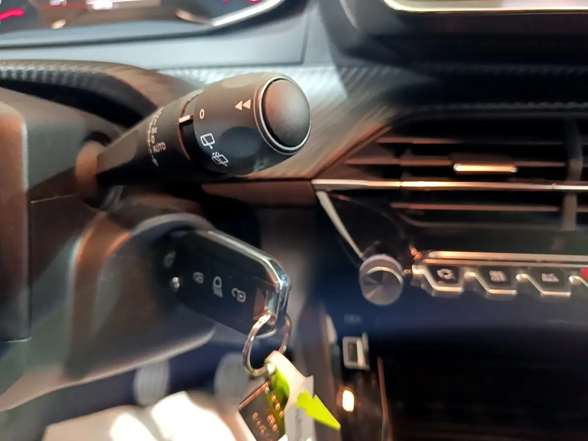 Gros plan intérieur sur la clé insérée et la commande d’essuie-glace du Peugeot 2008 gris clair, tableau de bord partiellement visible.