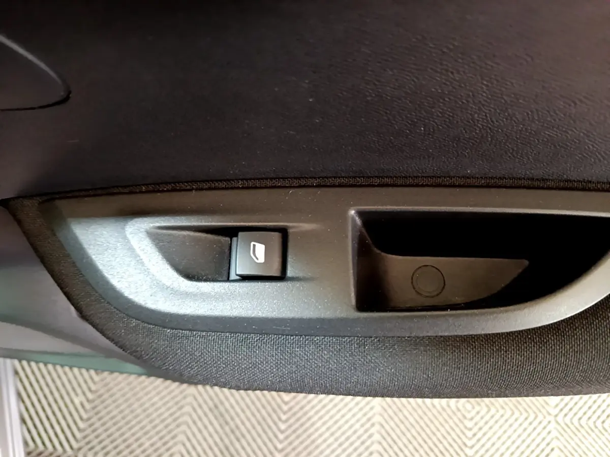 Bouton de commande de lève-vitre sur la porte intérieure côté gauche d’un Peugeot 2008 gris clair.